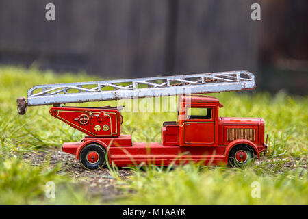 Old metal red fire engine toy made of tin in outdoor setting with grass Stock Photo