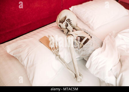 Human skeleton with mobile phone in hand lies in bed, black humor, funny joke Stock Photo