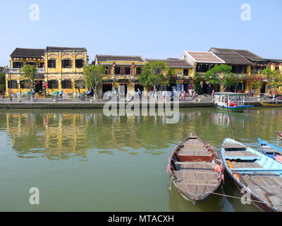 HOI AN, VIETNAM - 19TH MARCH 2018: Beautiful day in Hoi An ancient town with view of traditional boats, yellow houses by the river, and tourists Stock Photo