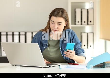 Intern working with a smart phone and a laptop on a desktop at office Stock Photo