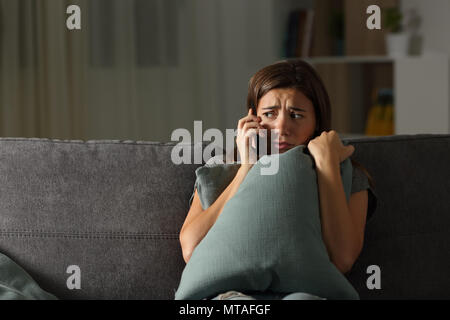 Scared teen calling police sitting on a couch in the living room at home Stock Photo