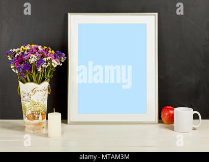 Silver frame mockup with field flowers in vase, apple, mug and candle. Empty frame mock up for presentation design. Template framing for modern art. Stock Photo