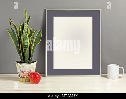 Silver frame mockup with plant pot, mug and apple on wooden shelf. Empty frame mock up for presentation design. Template framing for modern art. Stock Photo