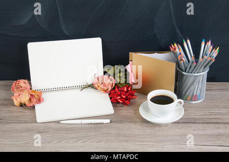 Blank opened notepad with copyspace; cup of coffee; stack of pencils; roses and greeting card on wooden background Stock Photo