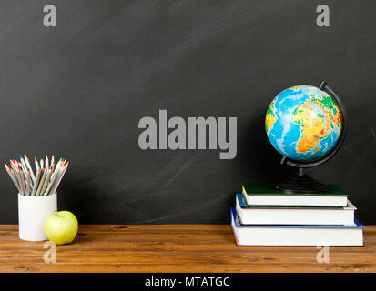 School supplies with stack of books and an apple on blackboard background with copyspace for your text, design. Back to school concept Stock Photo