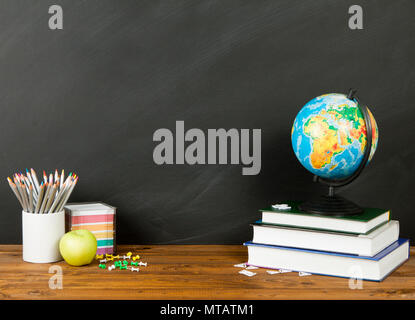 School supplies with globe, pencils, stack of books and an apple on blackboard background with copyspace for your text, design. Back to school concept Stock Photo