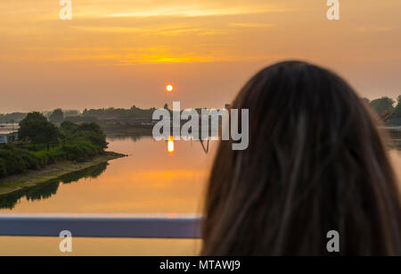 A woman watching the sun going down over a river in Summer in the UK. Stock Photo