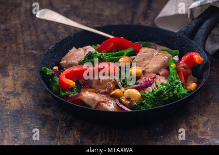 Sichuan pork, broccoli, red pepper and cashew stir-fry in a frying pan Stock Photo