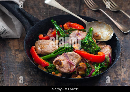 Sichuan pork, broccoli, red pepper and cashew stir-fry in a frying pan Stock Photo