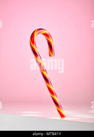 Colorful candy cane falling down near the edge of a white table on pink background Stock Photo