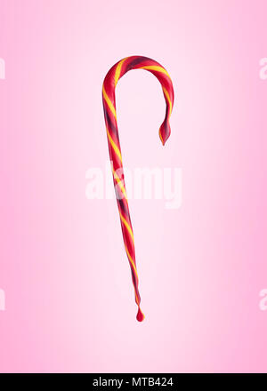 Colorful candy cane melting and dripping on pink background. Concept of melting and deformation. Stock Photo