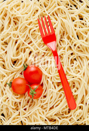 Red plastic fork and cherry tomatoes on a heap of cooked pasta spaghetti background. Top down view. Stock Photo