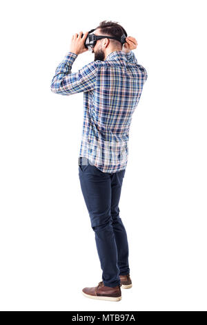 Young bearded smart casual man putting on virtual reality glasses headset on head. Full body isolated on white background. Stock Photo