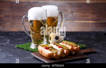 Photo of two mugs of foam beer, green grass with football, hotdogs Stock Photo
