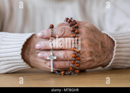 Close-up of senior's hands holding a red rosary with silver cross Stock Photo