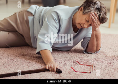 Sick senior woman with headache lying on the floor after falling down Stock Photo