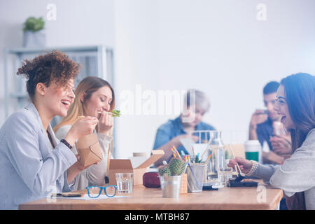 Caucasian employees eating lunch with their mulatto coworker Stock Photo