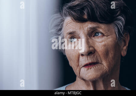 Portrait of despair, old woman standing beside window Stock Photo