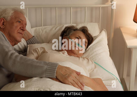 Man lying on bed next to elderly dying sick wife Stock Photo