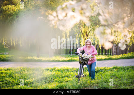 Beautiful senior woman with bicycle outside in spring nature. Stock Photo