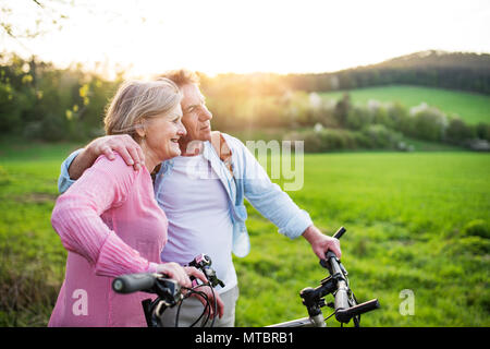 Beautiful senior couple with bicycles outside in spring nature. Stock Photo