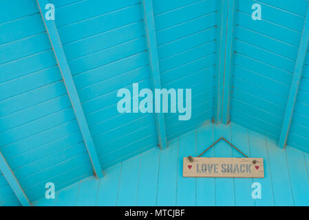 Love shack written in hand painted words on a wooden panel board attached under the roof of a pastel light blue wooden cabin Stock Photo