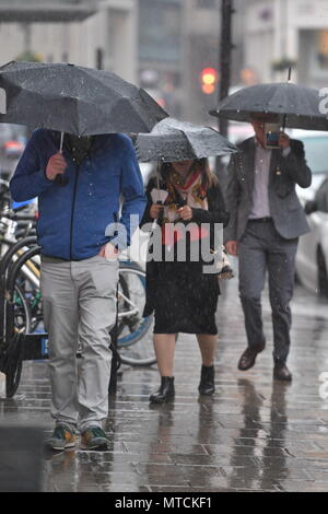 People get caught in a downpour in Victoria, central London, as forecasters have warned of the risk of more flooding, travel disruption and power cuts with thunderstorms set to rumble on. Stock Photo