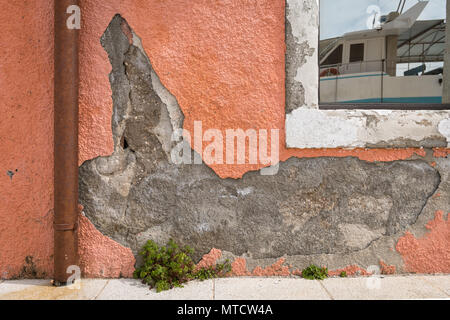 Crumbled plaster of an orange wall, reflection of a boat in the window, harbour in Cres (Croatia) Stock Photo