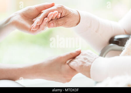 Close-up of a young woman and a senior lady holding hands with tenderness and care. Showing support and love. Blurred background. Stock Photo