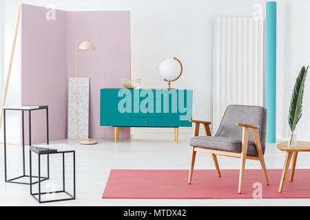 Wooden turquoise cupboard with gold bowl and white globe standing in pastel colors room interior with grey chair and metal lamp in the corner Stock Photo