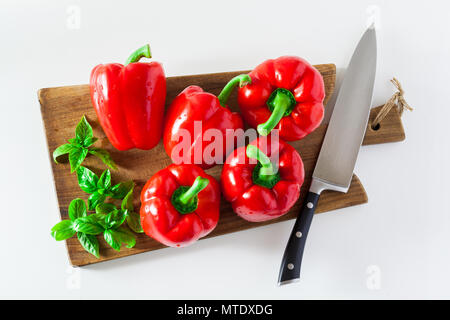 a group of red ripe organic peppers and fresh basil leaves on a cutting board and a knife. Stock Photo