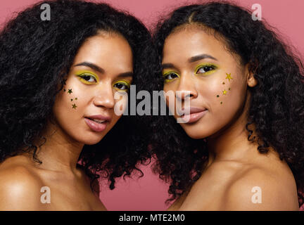 Two young women with fashion make up standing together in studio over pink background Stock Photo