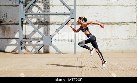 Full length shot of young female athlete sprinting in city. Slim woman running in the morning. Stock Photo