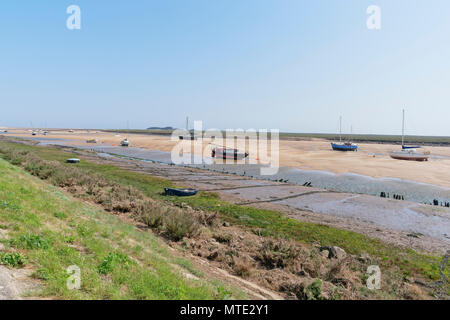 From the top of a grass bank, looking out over boats beached on sandbanks to the flat marshes at Wells-next-the-Sea Stock Photo