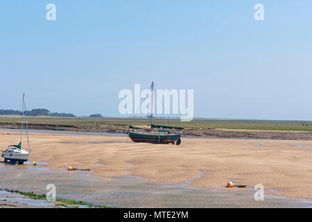 An old yacht sits on a sandbank at low tide in an estuary. Salt marshes stretch out in to the distance Stock Photo