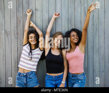 Three young women having fun near wall outdoors Stock Photo