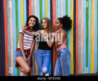 Group of women taking selfie with mobile phone, standing on city street at colorful wall Stock Photo