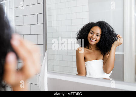 Young woman standing in bathroom, holding her curly hair Stock Photo