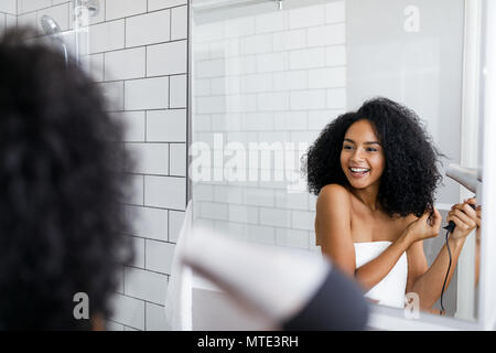 A young woman blow drying her hair in front of a mirror Stock Photo