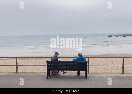 Couple sitting apart on a bench overlooking the beach at Lyme Regis Dorset England UK Stock Photo