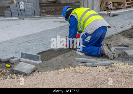 Builder worker installing the pavestone on the sidewalk,  laying paving stones. Stock Photo