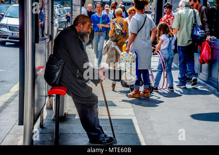 A man sits in a bus shelter in Hammersmith, London begging for money with a hat. Stock Photo