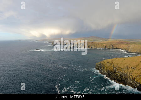 High up cliff shots of the sea and land in Shetland with a storm and a rainbow and choppy seas Stock Photo