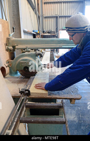 Workman in a workshop working a chop saw cutting a piece of wood for constructing a house kit Stock Photo