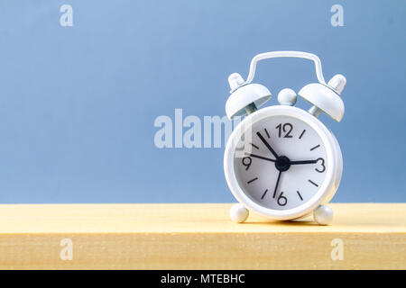 White small alarm clock on a wooden shelf on a grey pastel background. Minimalism Stock Photo