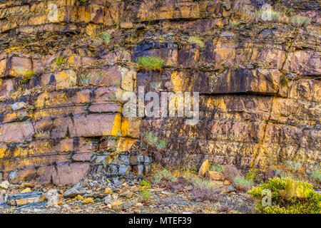 Natural colourful rockface background in Andalucia, Spain. The rock is flat and layered, it is crumbling in places, slate like.  It has yellow and blu Stock Photo
