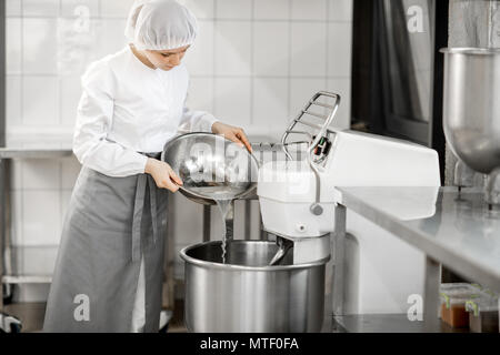 Woman mixing ingredients in the kneader machine standing at the bakery manufacturing Stock Photo