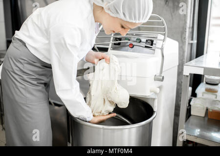 Woman mixing dough with professional kneader machine at the manufacturing Stock Photo