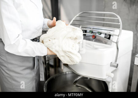 Woman mixing dough with professional kneader machine at the manufacturing Stock Photo