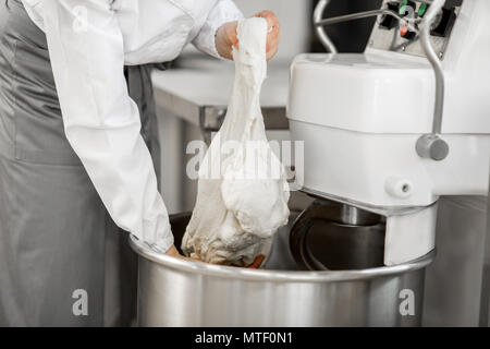 Woman mixing dough with professional kneader machine at the manufacturing Stock Photo